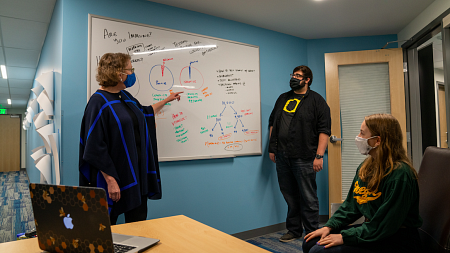 Three people conversing in front of white board with plans for coronavirus information story. 