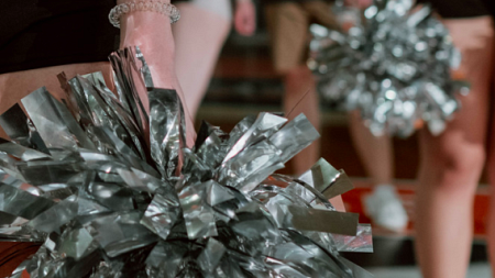 A cheerleader wearing a black uniform holds a pom-pom at their side while in formation with other cheerleaders (Ron Lach from Pexels).
