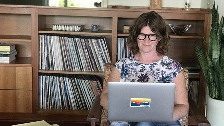 Kathryn Kuttis types on her grey laptop with an Oregon sticker in front of a record shelf.