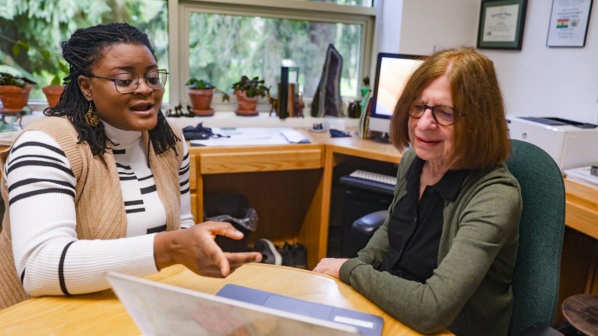 Ivy Fofie and Leslie Steeves sit at a small table in an office looking at a laptop screen