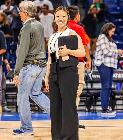 Carly Ebisuya holds a clipboard while standing in the middle of a basketball court