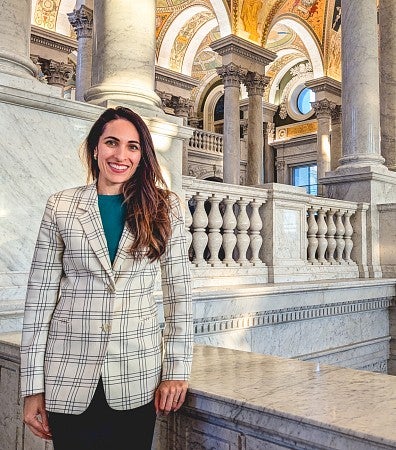 Priya Sage poses in front of grand marble columns and balustrades and an ornate ceiling