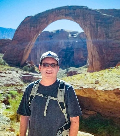 Daniel Zweifach poses in front of a natural stone arch