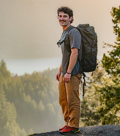 Dan Teitelbaum stands at the top of a rock ledge with a hazy mountain scene behind him