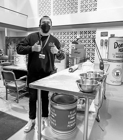 black and white photo of Nolan Biorn wearing a face mask and posing in a set kitchen