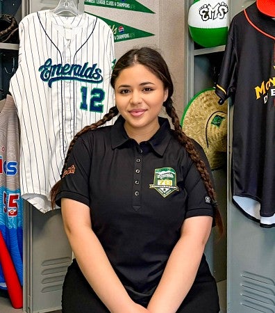 portrait of Sarah Ortiz taken in the Eugene Emeralds locker room where she is surrounded by Emeralds' gear