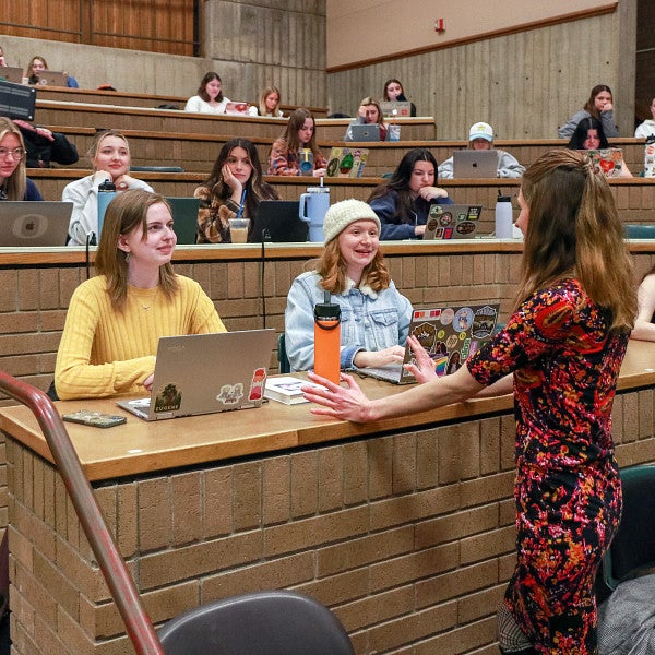 Whitney Phillips speaks to two students in a large classroom