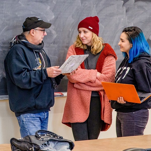 Dave Koranda holds a laptop and talks to two students