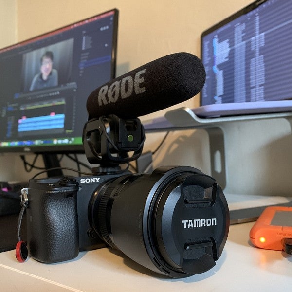 A Sony camera sits on a desk in front of a computer screen showing the video editing process.