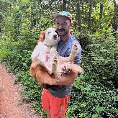 John Sutter holds a dog in his arms while on a hiking trail