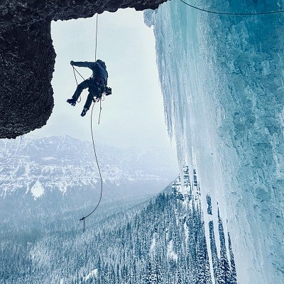 Dan Teitelbaum hangs from rock climbing ropes high above an icy forest