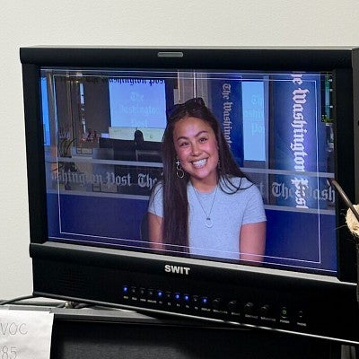 a screen monitor shows Sydney Seymour sitting at a Washington Post TV news desk