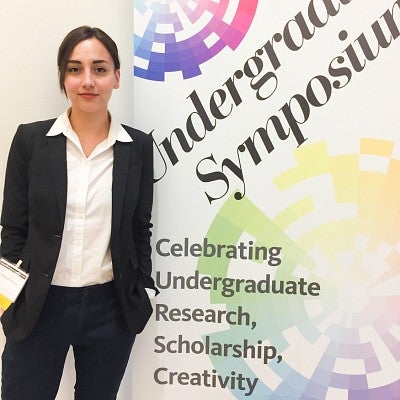Francesca Fontana stands next to a large banner that says "Undergraduate Symposium; Celebrating Undergraduate Research, Scholarship, Creativity"